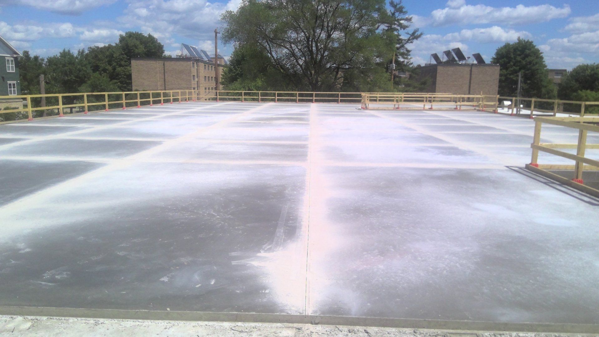 Flat, concrete construction site with safety railings, covered in white powder. Buildings and trees in background.