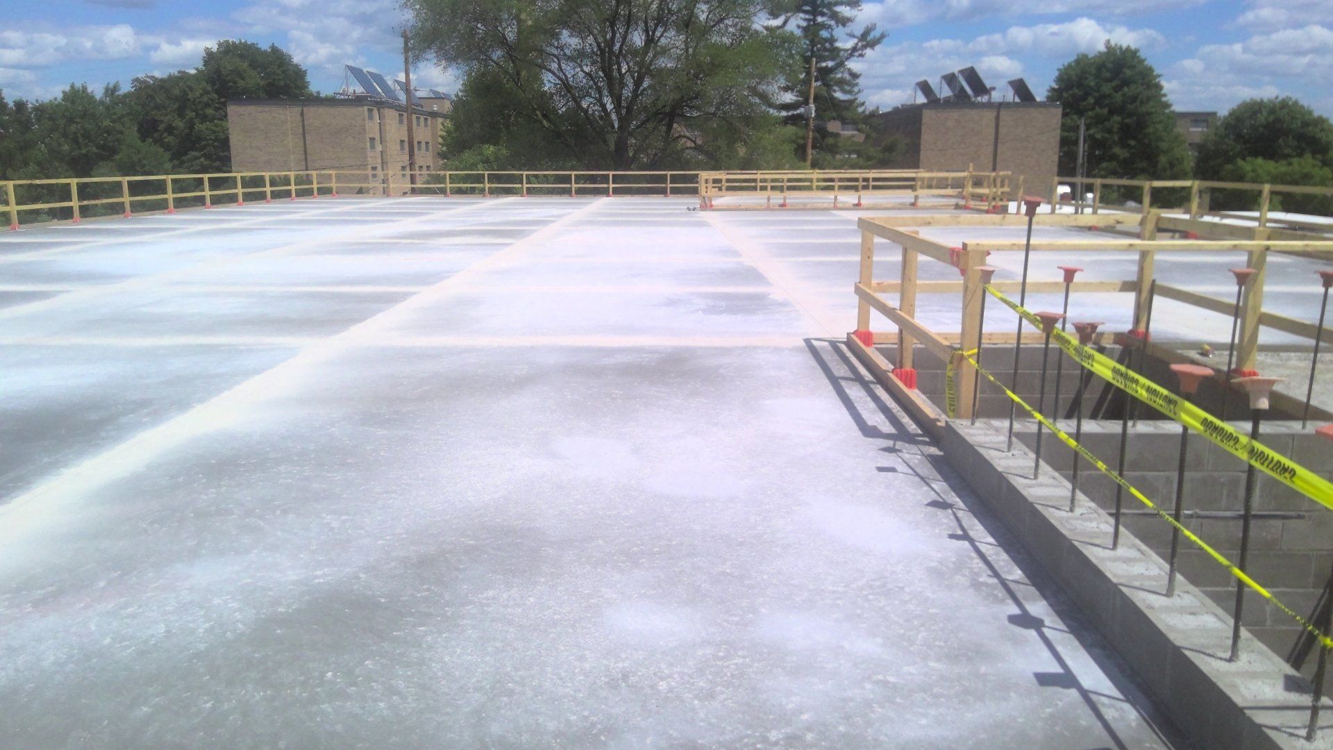 A concrete construction site with temporary wooden guardrails. Bright sunny day.