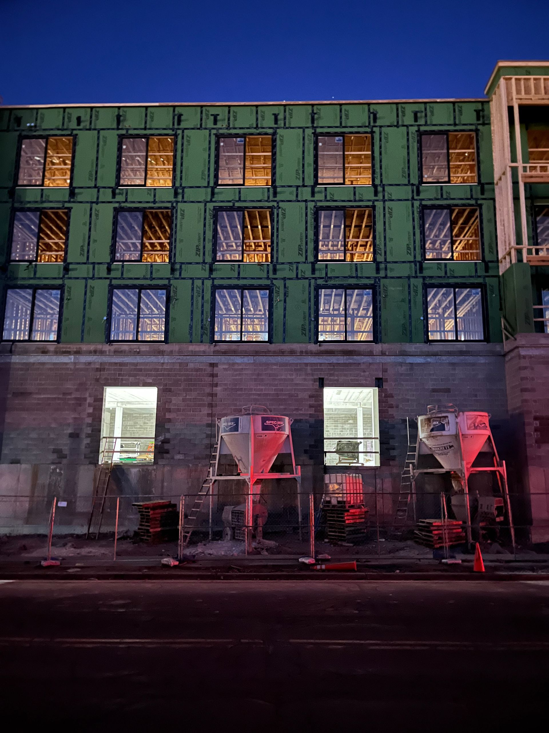 Building under construction at night, with illuminated windows and construction equipment.