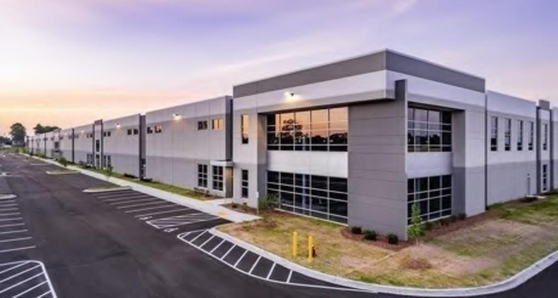 Modern, gray and white commercial building with glass windows, asphalt parking area.