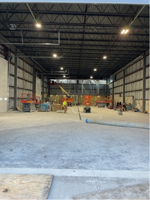 Interior of a warehouse under construction, with workers, equipment, and exposed steel beams.