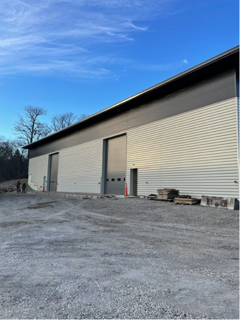 Gray industrial building with two overhead doors on a gravel lot under a blue sky.