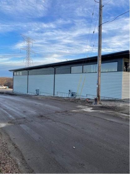 Exterior of a light blue metal-clad building with a dark roof and windowed upper level, a utility pole in front.