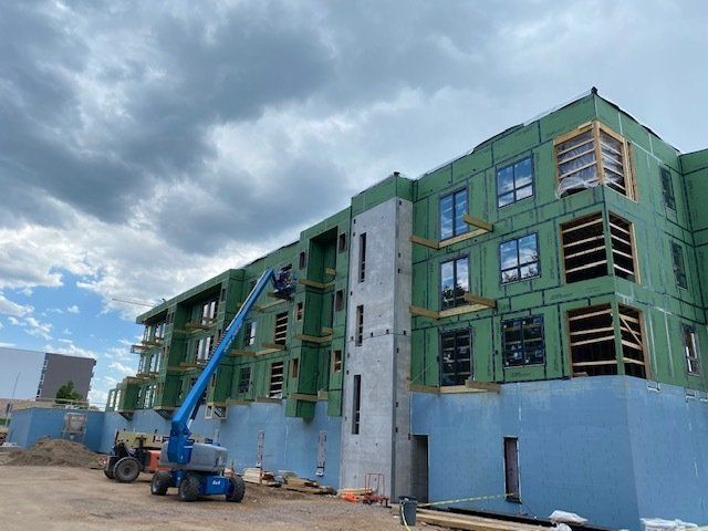 Building under construction with a blue lift and cloudy sky. Green and blue siding.