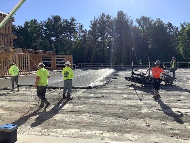 Construction workers pouring and leveling concrete at a building site on a sunny day.