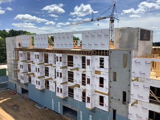 Building construction site with crane and partially built apartment complex under blue sky.