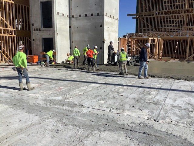 Construction workers pouring and smoothing concrete on a sunny day near a building under construction.