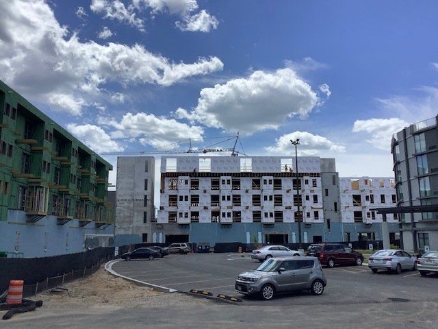 Construction site: multi-story buildings, parking lot, cars, cloudy sky.