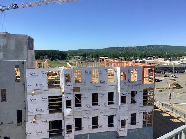 Construction of a multi-story building, exterior view. Blue sky, wooden frames, sheathing visible.