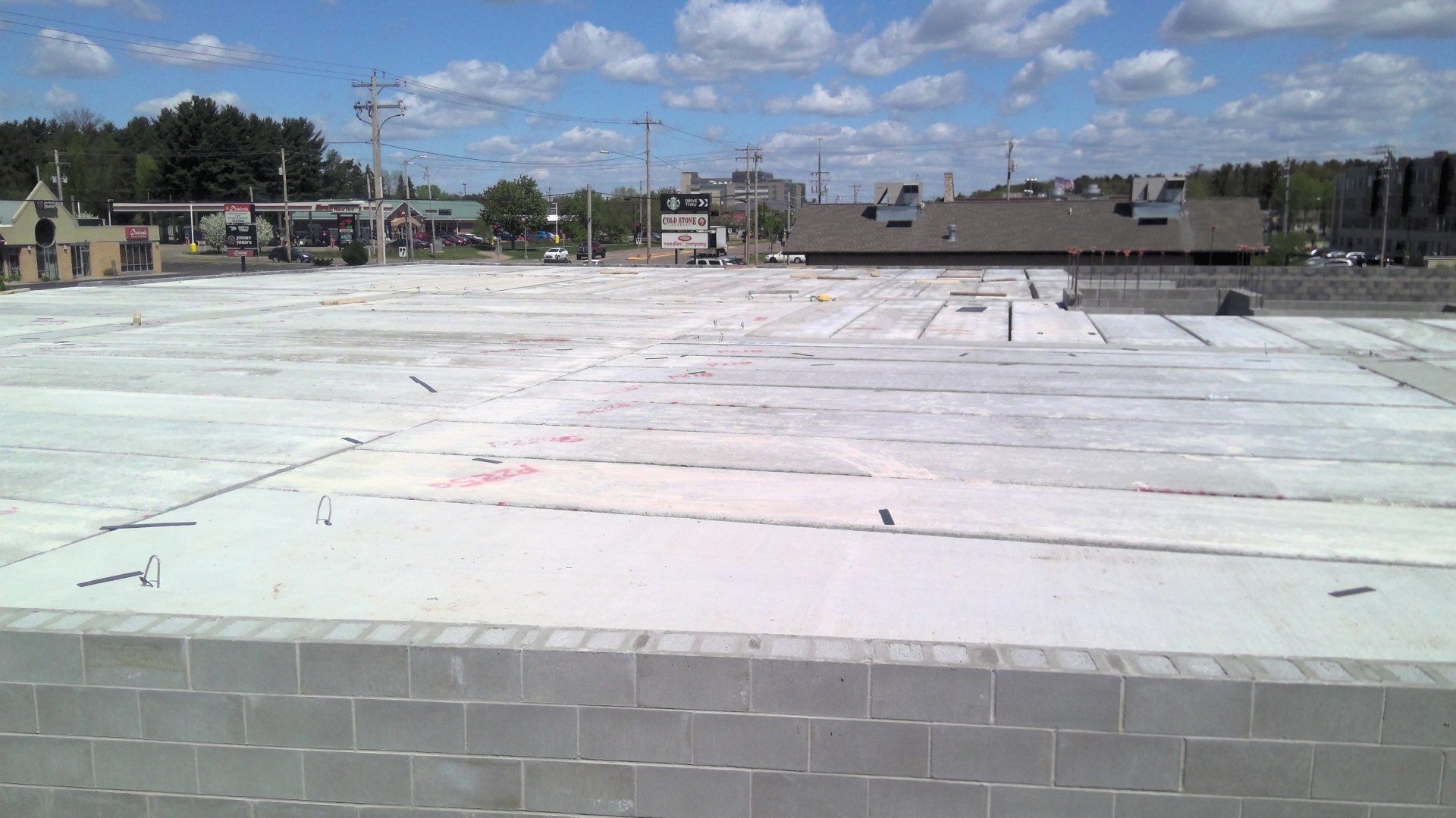 Large, empty concrete area, possibly a construction site, with buildings and a cloudy sky in the background.