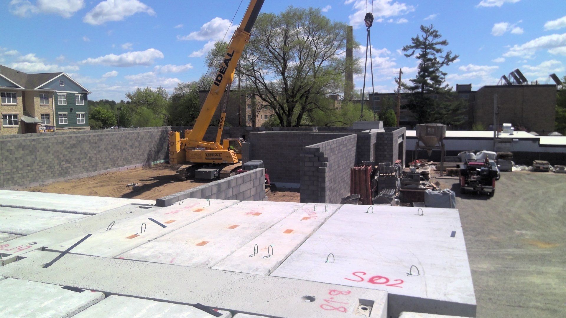Construction site with crane lifting blocks, unfinished building, concrete slabs, bright sunny day.