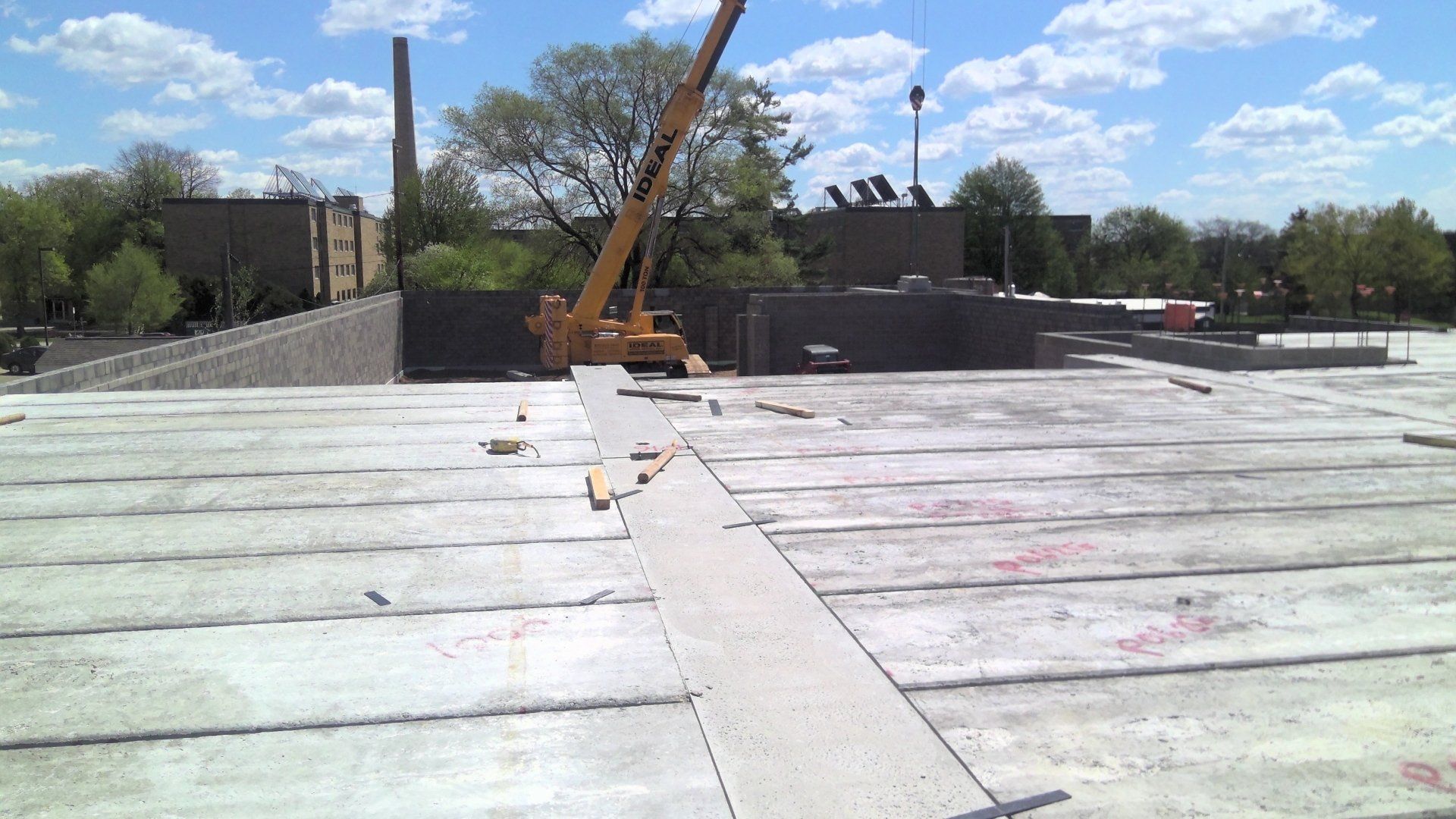 Construction site rooftop with precast concrete panels, crane, and buildings in the background.