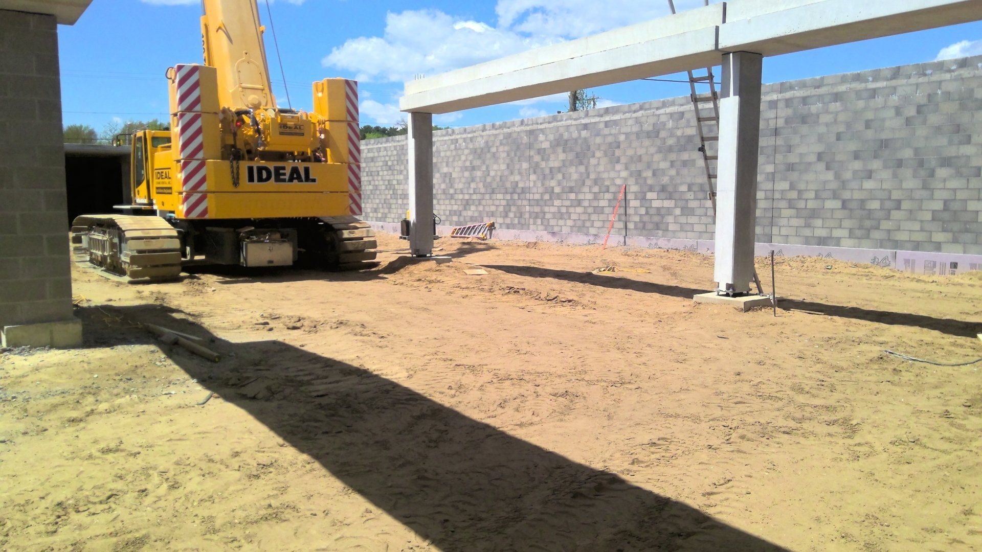 Yellow crane lifting concrete beams at a construction site with cinder block walls.