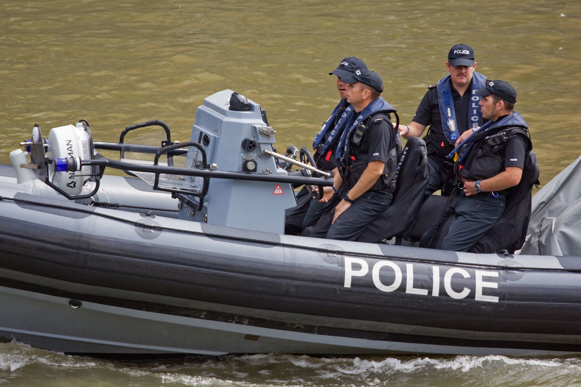 Police officers in a black and grey boat on water; the word