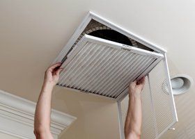A Person is Cleaning a Ceiling Vent With a Filter