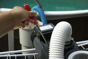 A hand using a red-handled screwdriver to open the electrical cover on a black pool pump motor.
