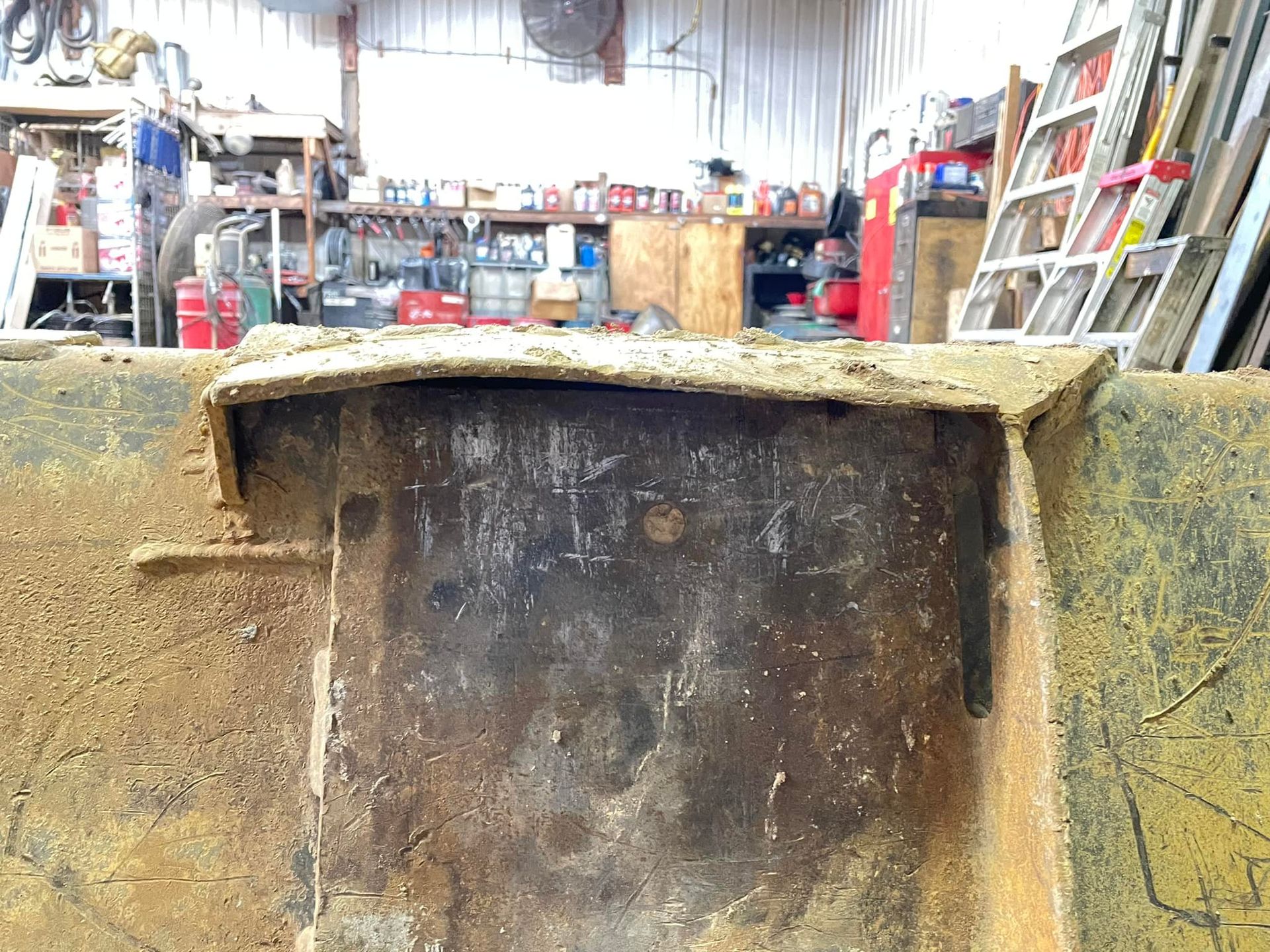 A dirty piece of metal in a garage with a ladder in the background