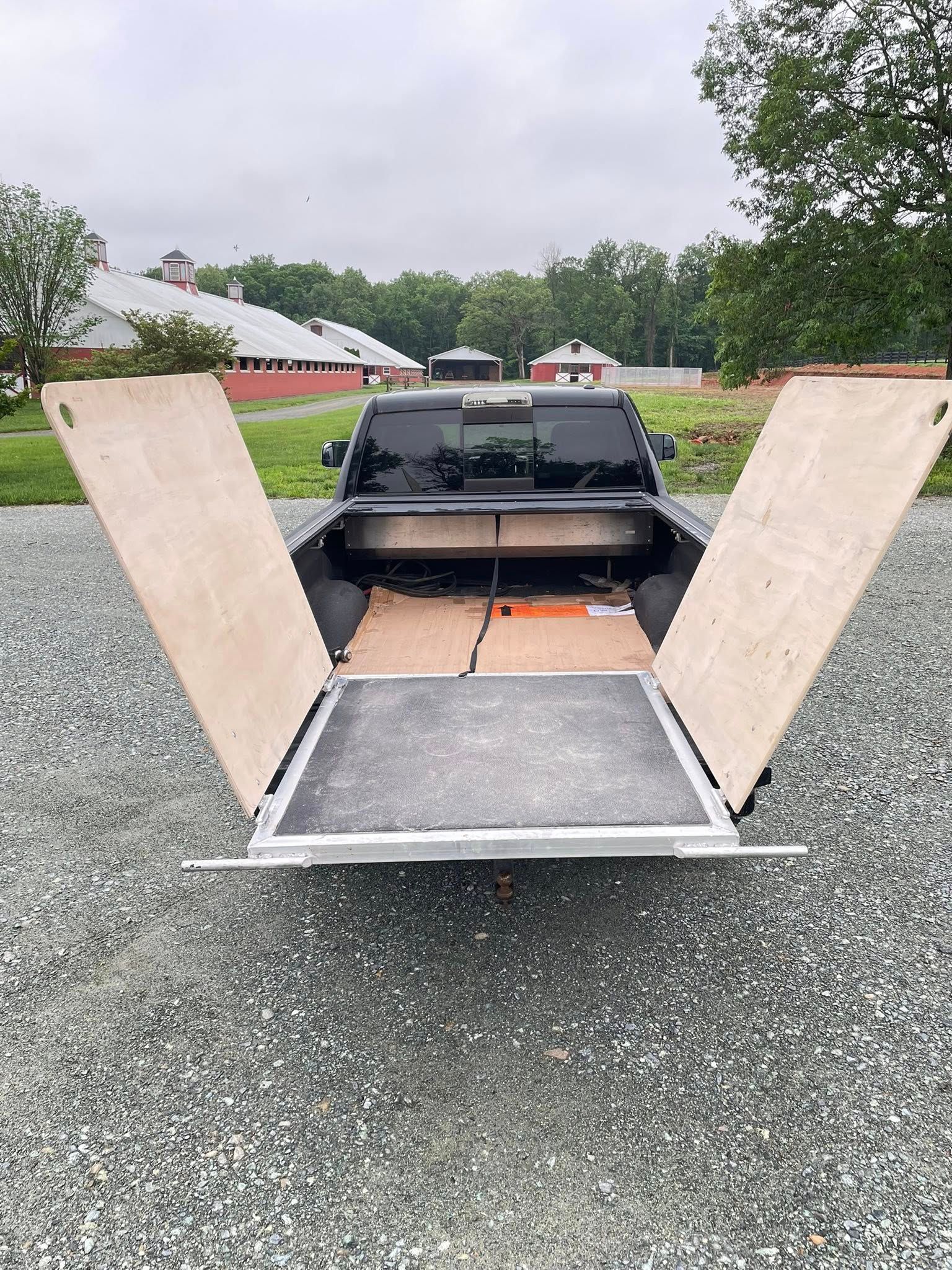 The back of a truck with the doors open is sitting on a gravel road.