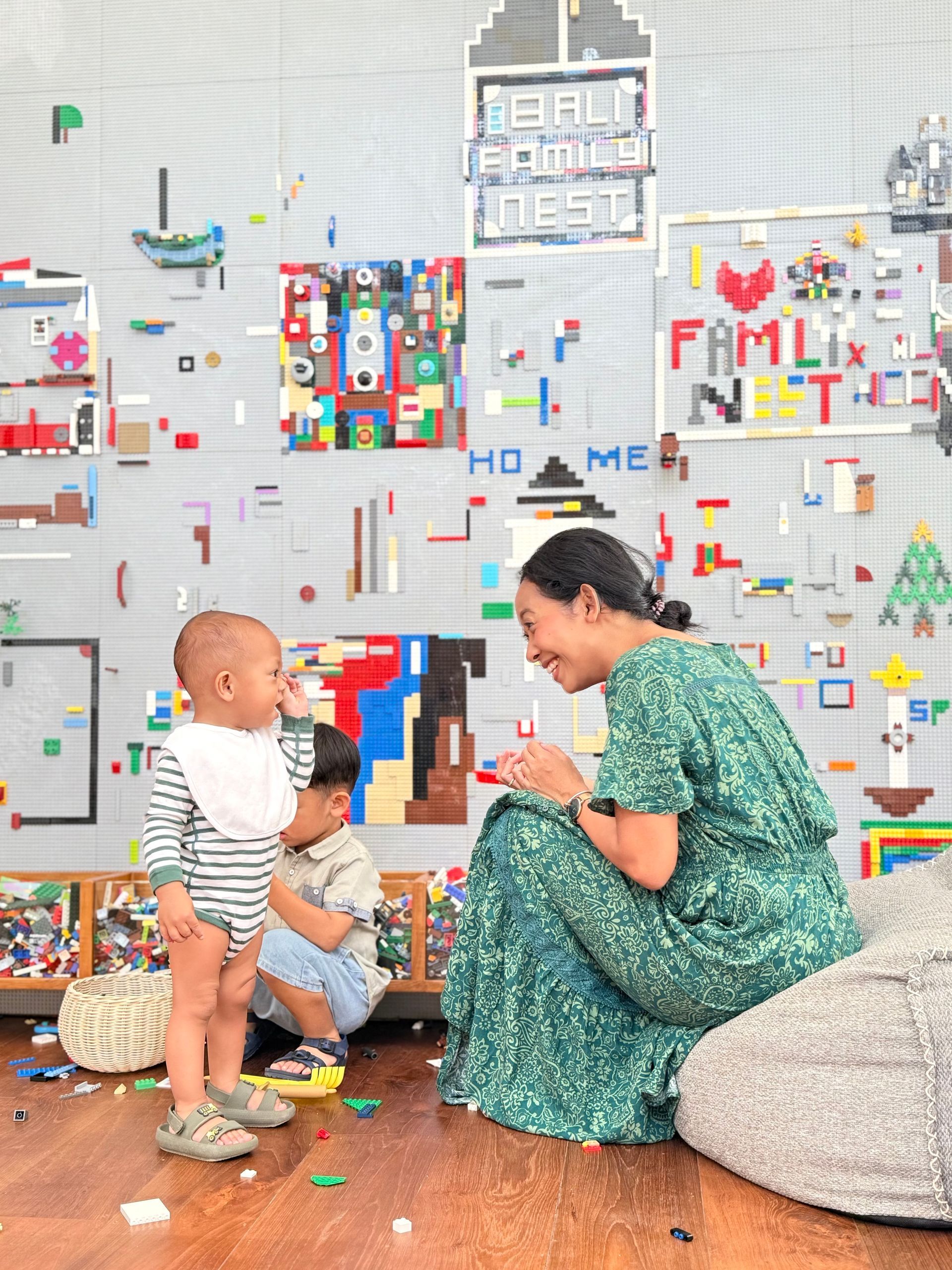 Parent and two children playing on a wooden floor in a bright room with colorful wall art.