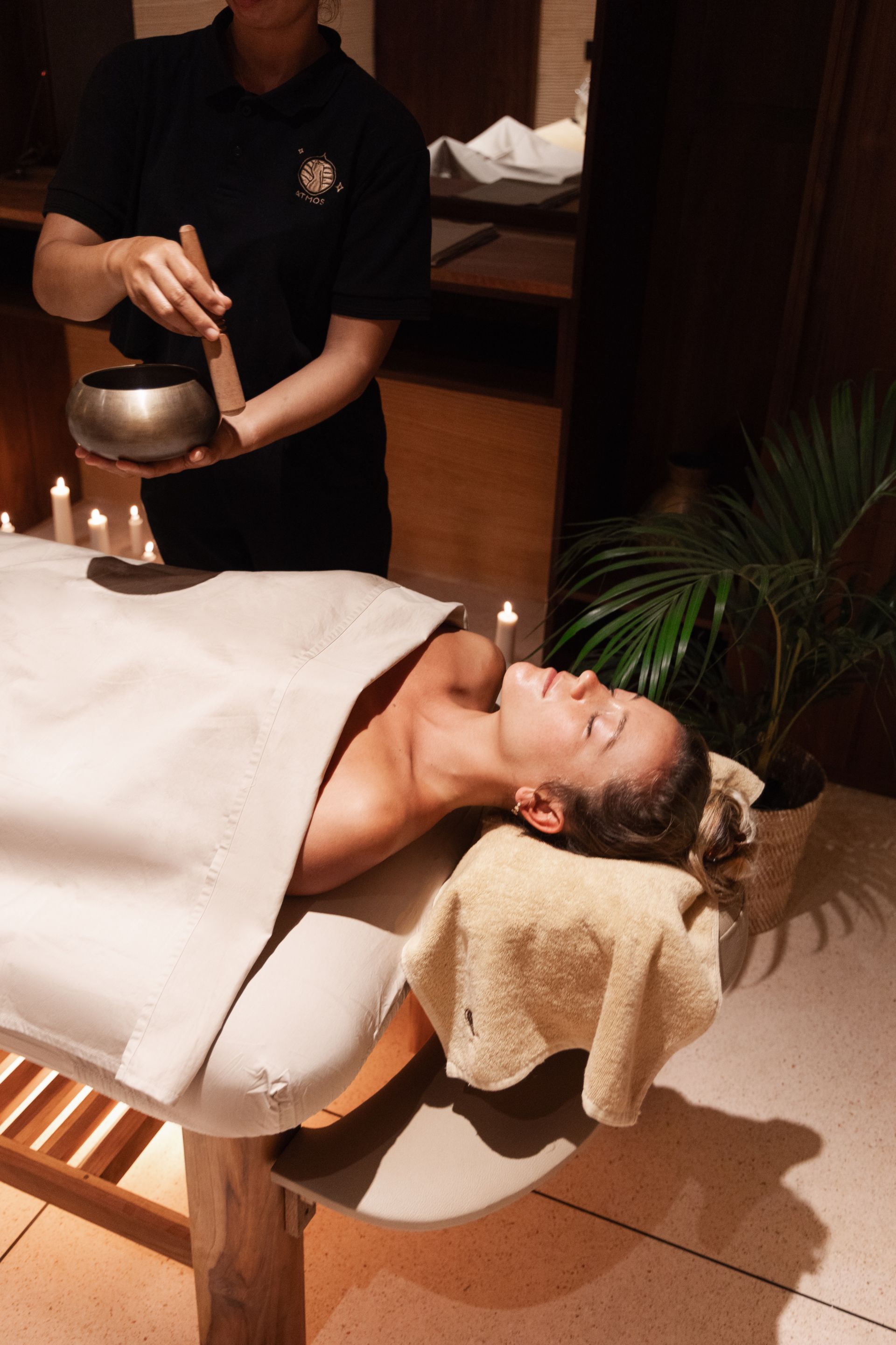 Spa massage therapist pouring liquid over a woman reclining on a treatment table