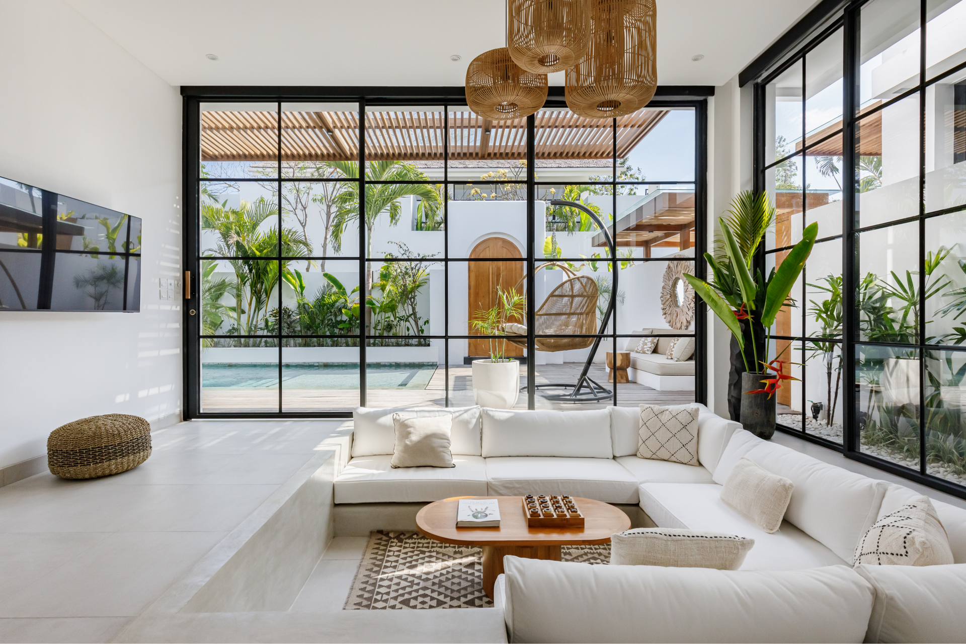 Bright modern living room with white sofas, large black-framed windows, plants, and an outdoor pool view