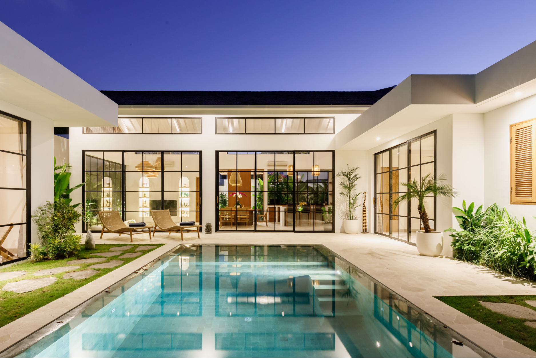 Modern courtyard home with a lit swimming pool and large glass doors at dusk