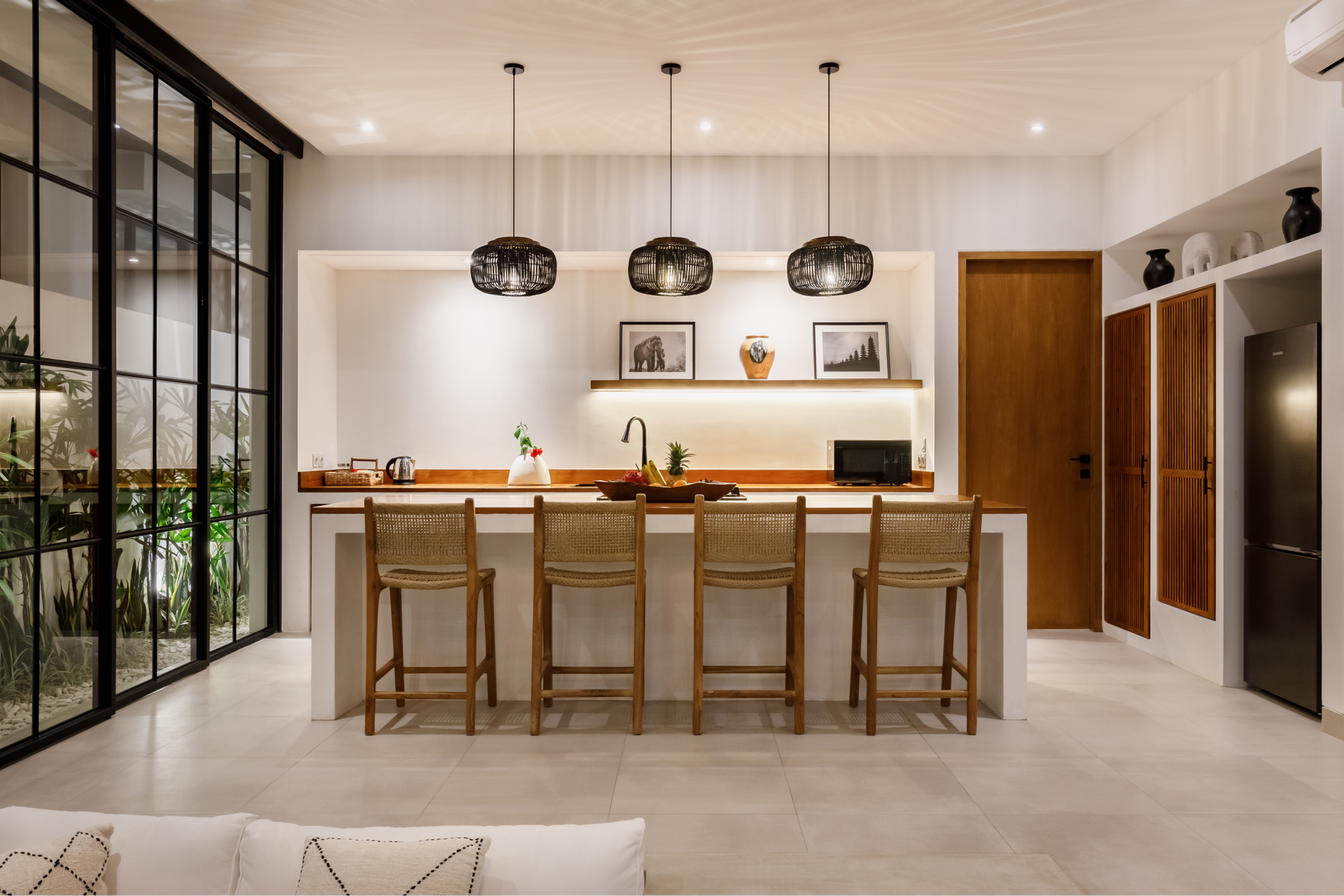 Modern kitchen with wood island, four stools, pendant lights, and large glass doors opening to greenery