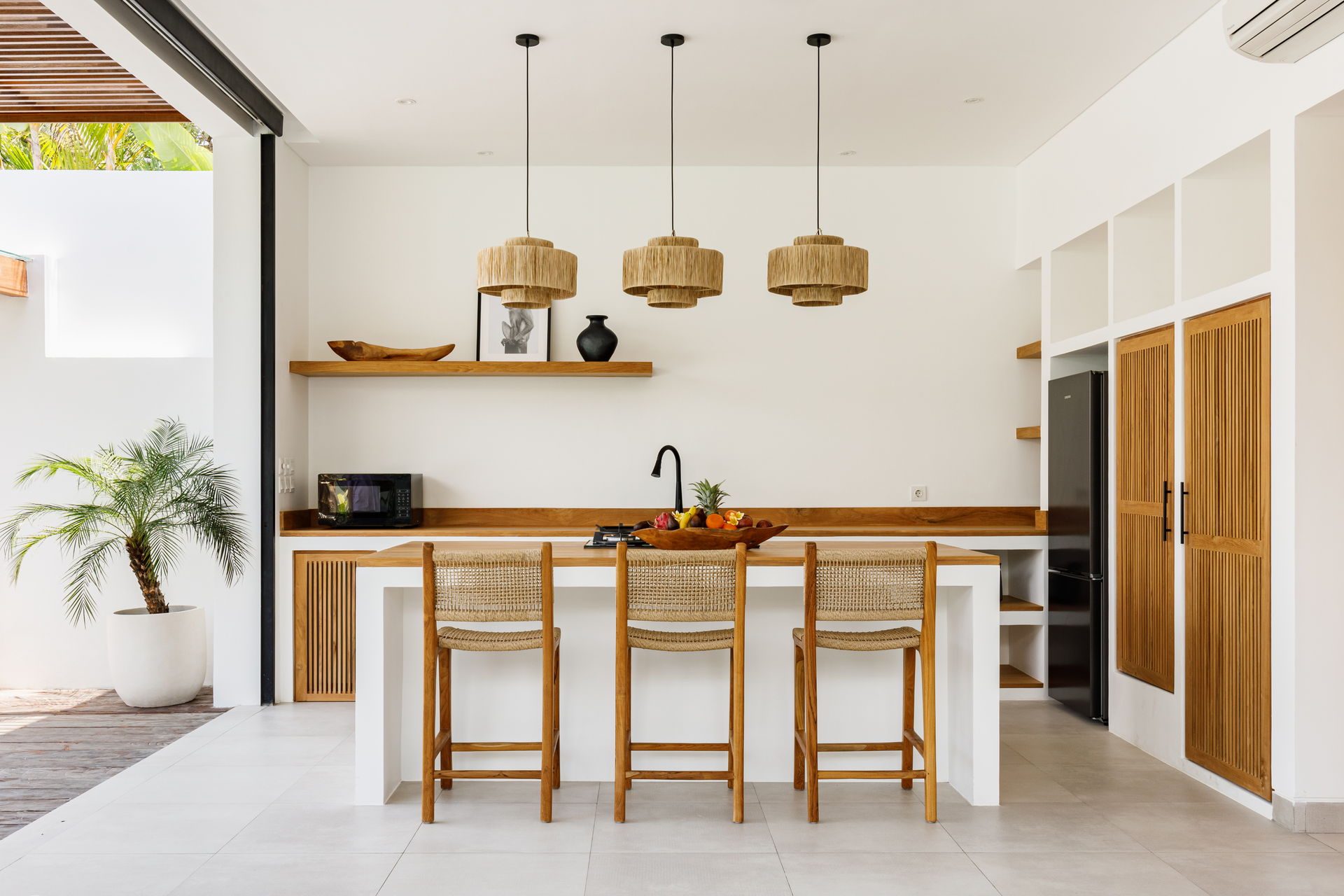 Bright modern kitchen with wooden island stools, woven pendant lights, and open shelving