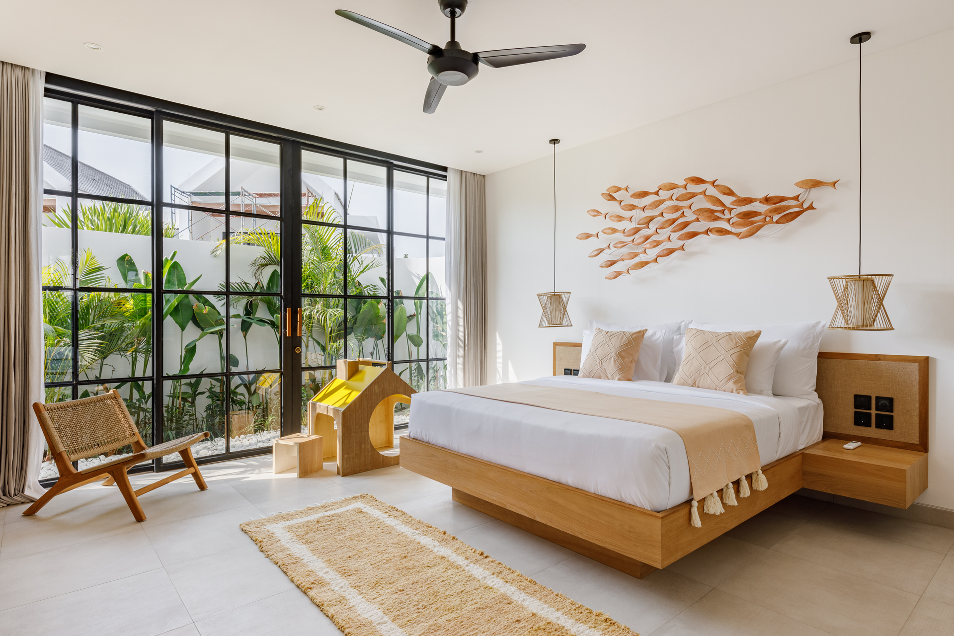 Bright modern bedroom with large windows, a wooden bed, woven chair, and ocean-themed wall art