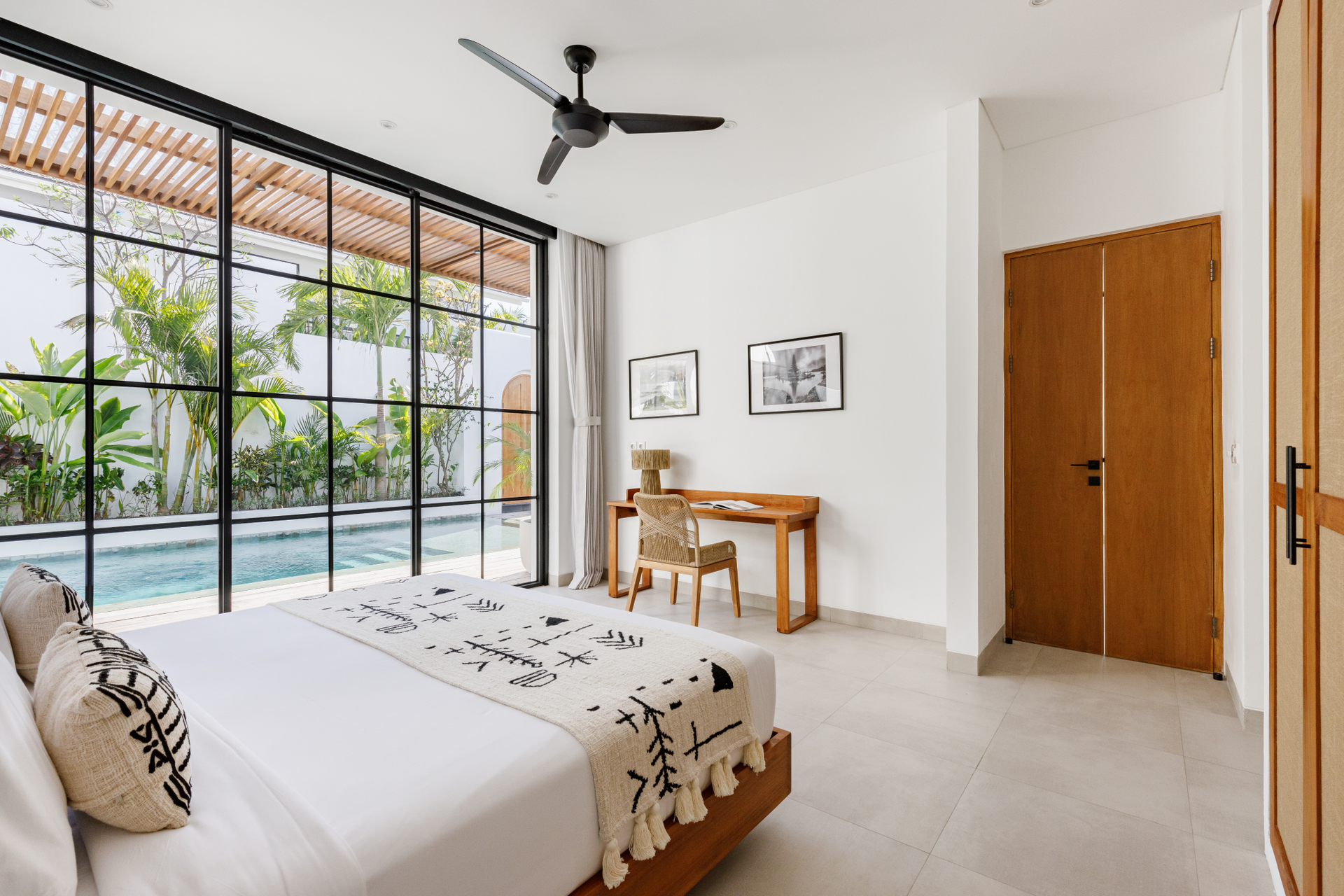 Bright bedroom with bed, desk, ceiling fan, and large sliding doors opening to a pool.