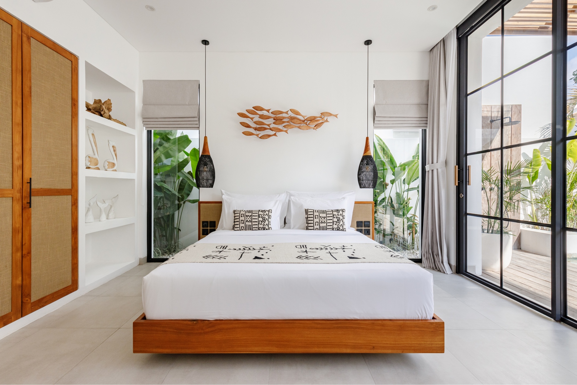 Bright modern bedroom with a low wooden bed, white decor, and large glass doors opening to greenery
