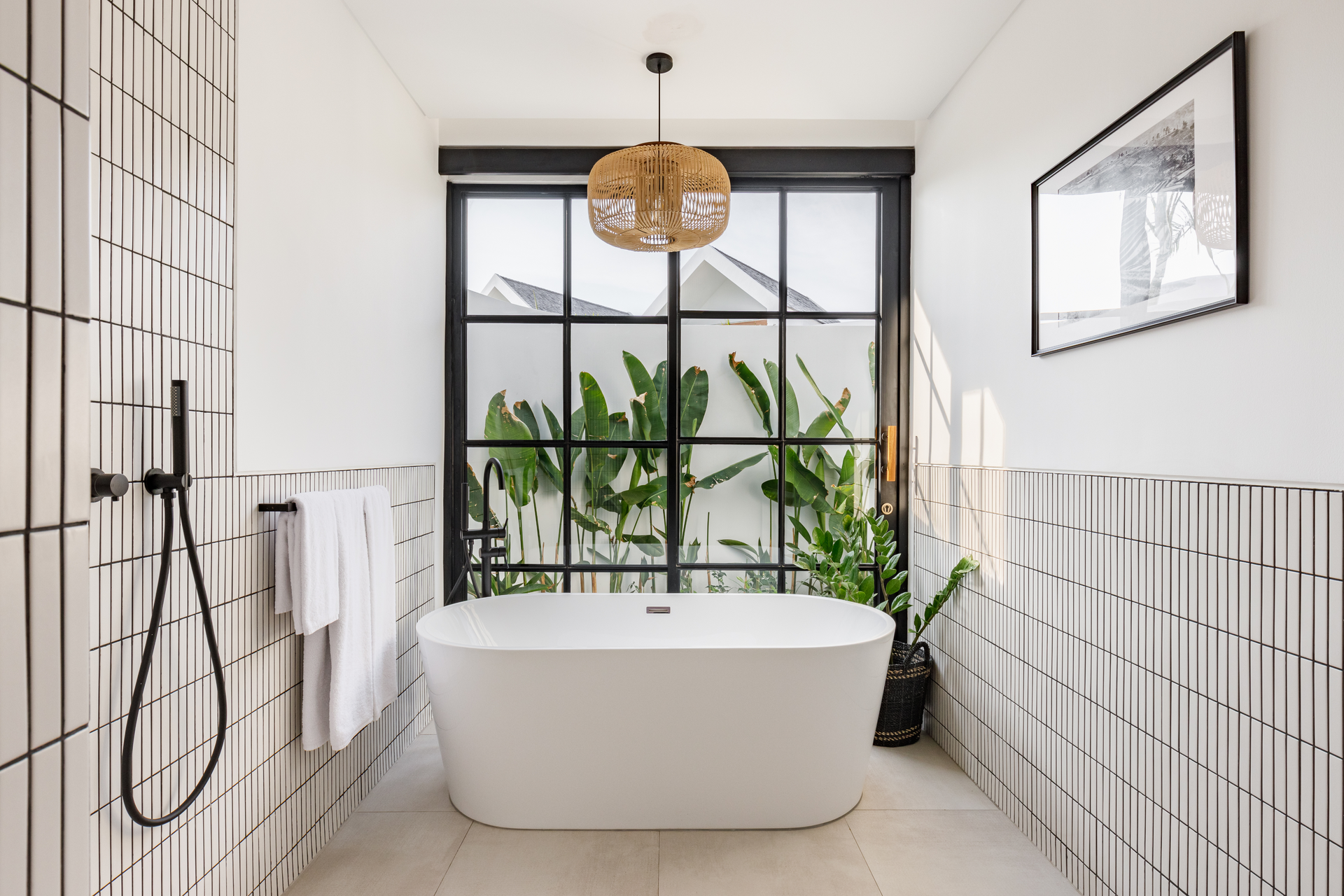 Modern bathroom with freestanding tub, black-and-white tile, and large window overlooking greenery