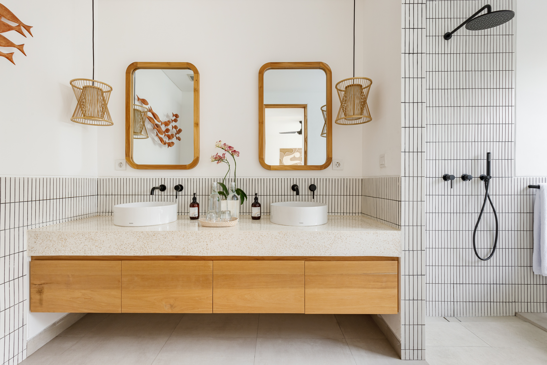Modern bathroom with wood vanity, double sinks, mirrors, and tiled shower wall