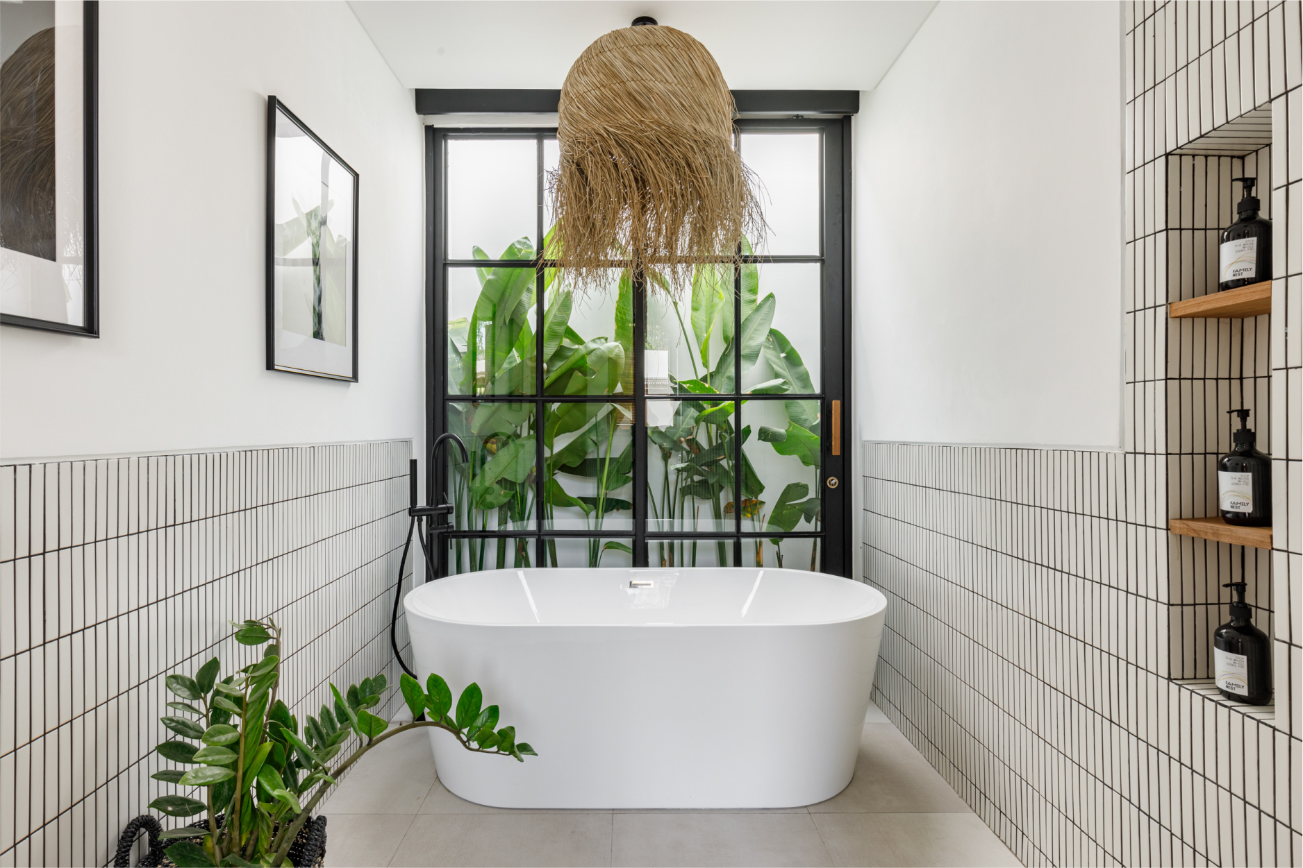 Modern bathroom with white freestanding tub, black-framed window, tiled walls, and hanging woven light fixture