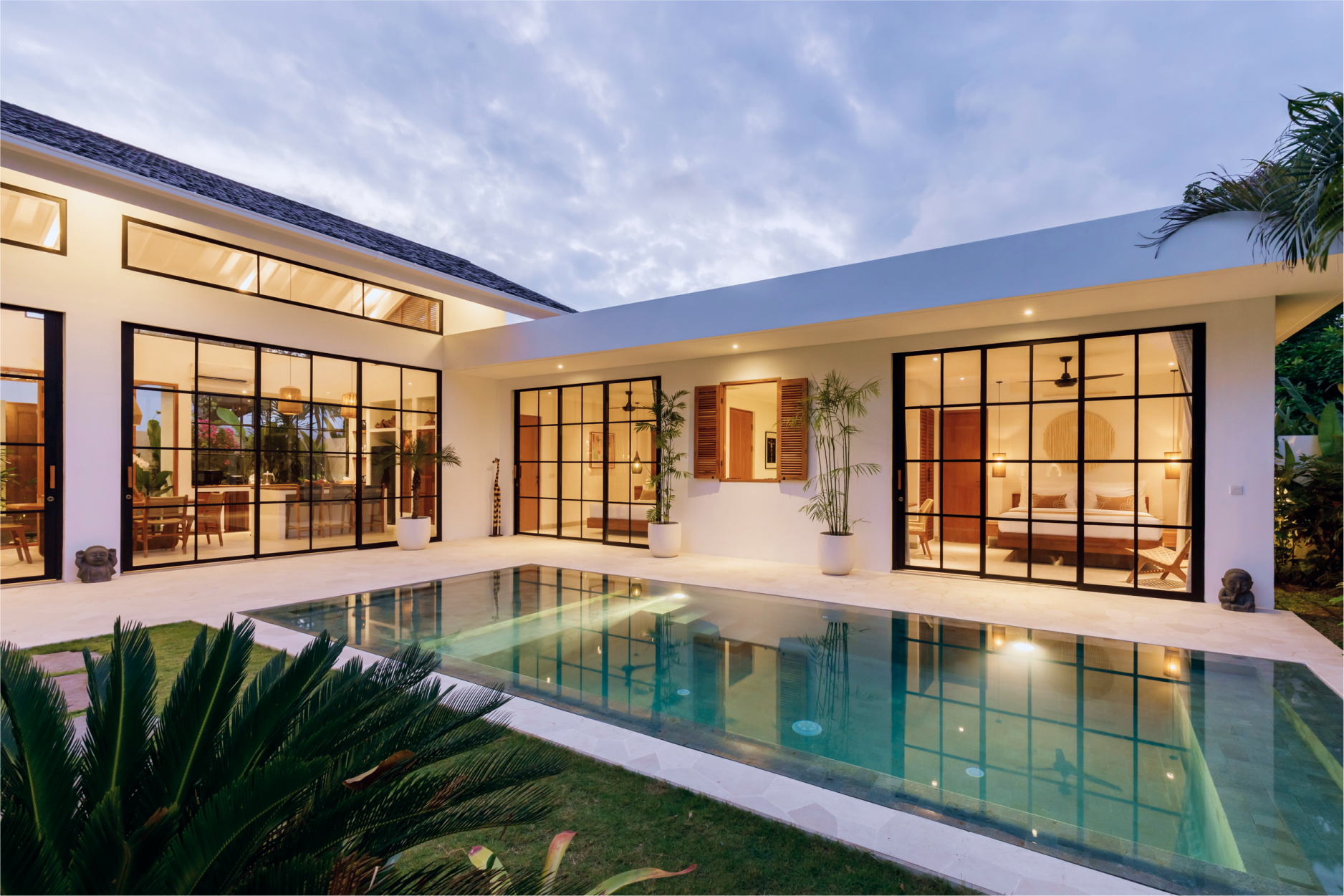 Modern white home with large glass walls and a turquoise pool at dusk