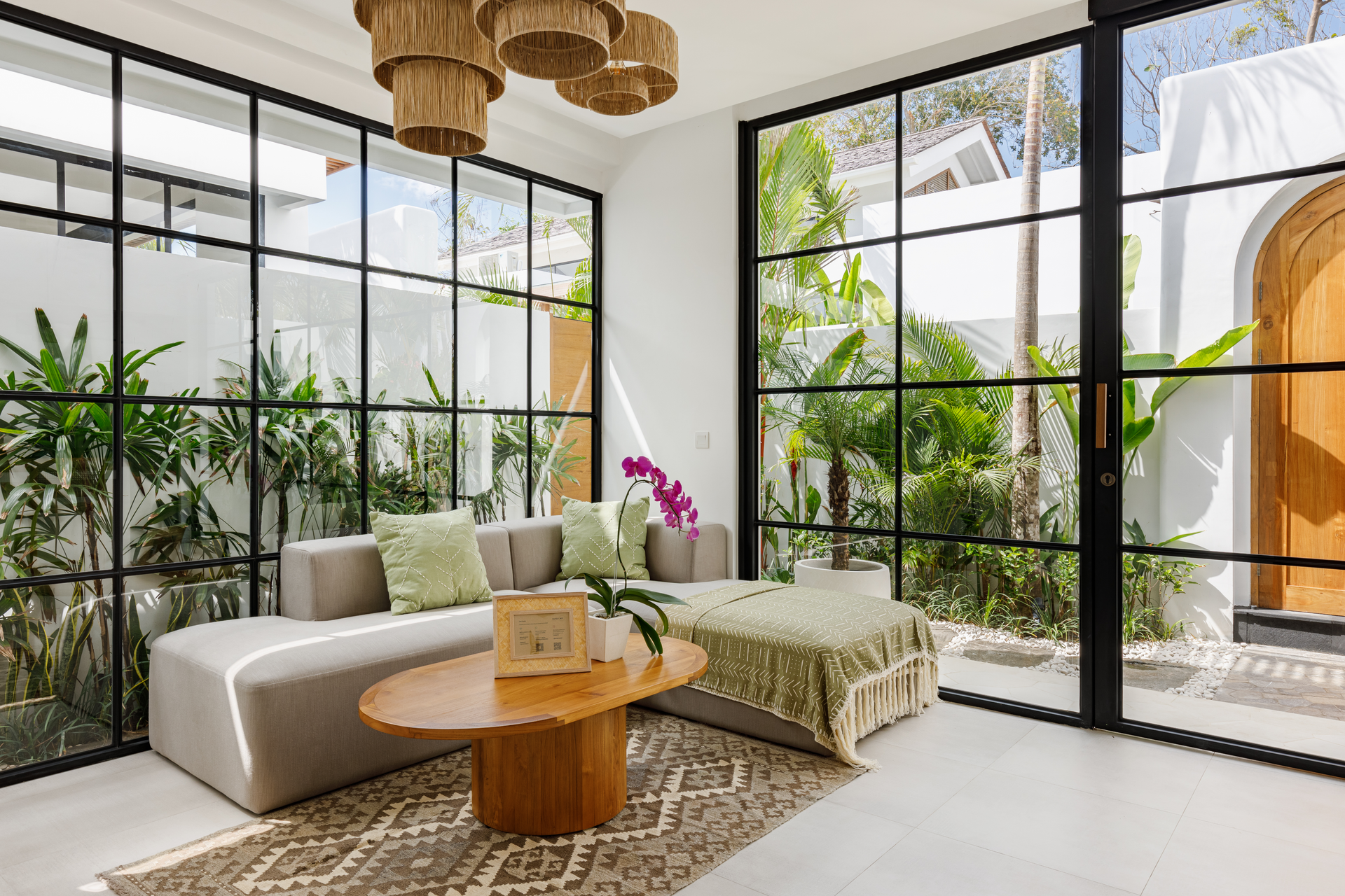 Bright modern lounge with sectional sofa, coffee table, hanging lights, and floor-to-ceiling garden windows