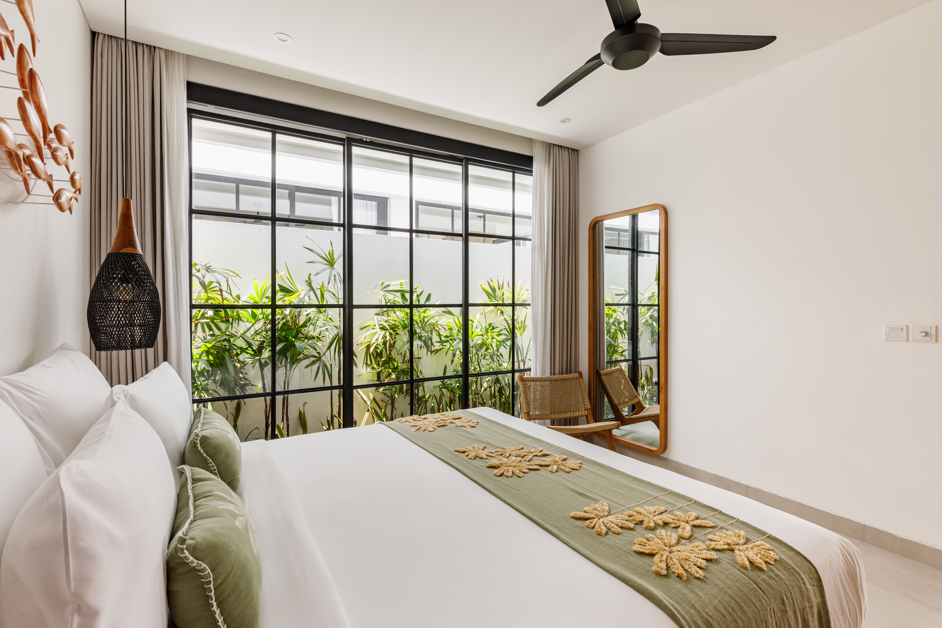 Bright bedroom with a large window, white bedding, green accents, and a ceiling fan