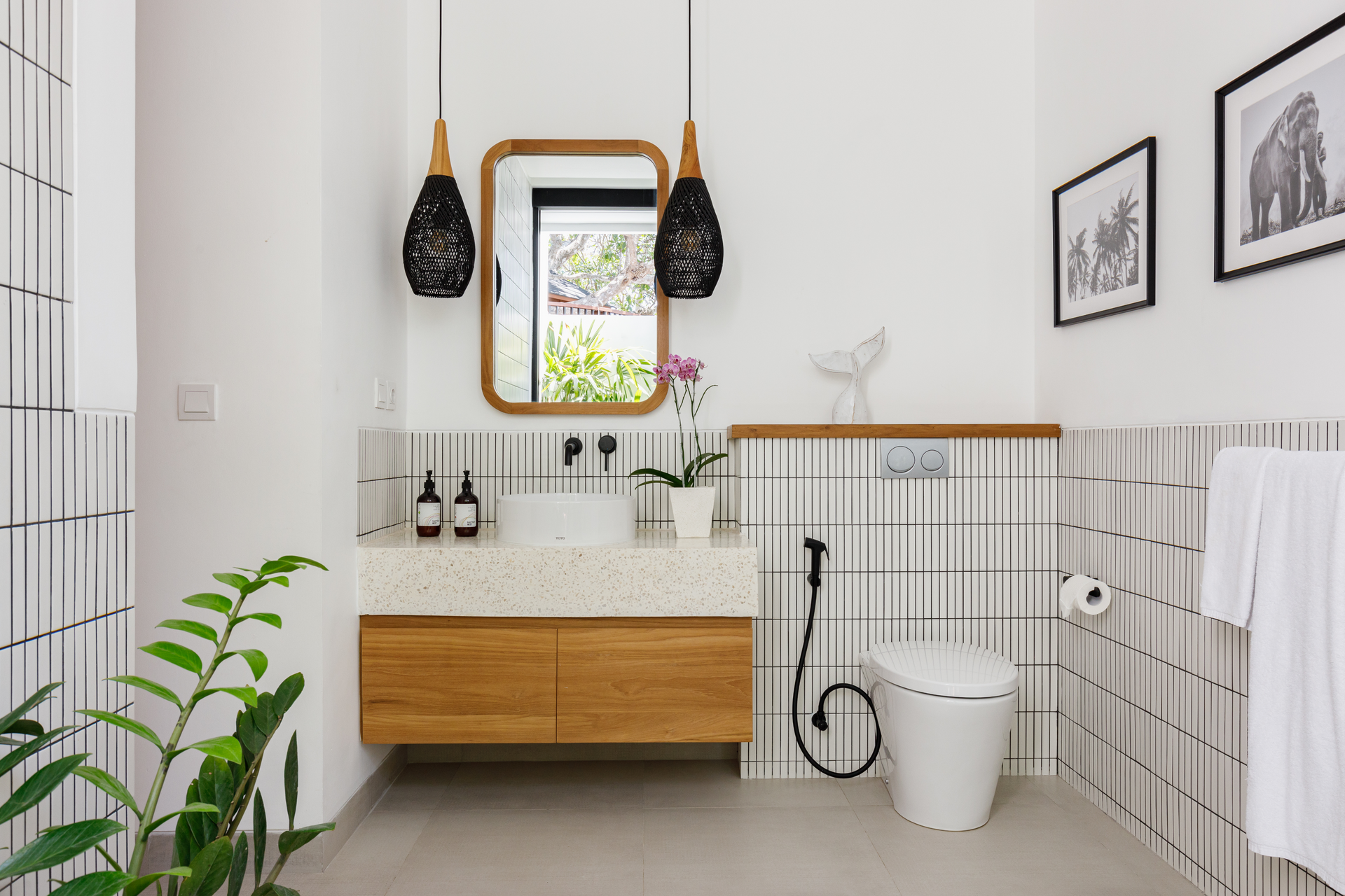 Bright white modern bathroom with wood vanity, black fixtures, tiled walls, and a potted plant
