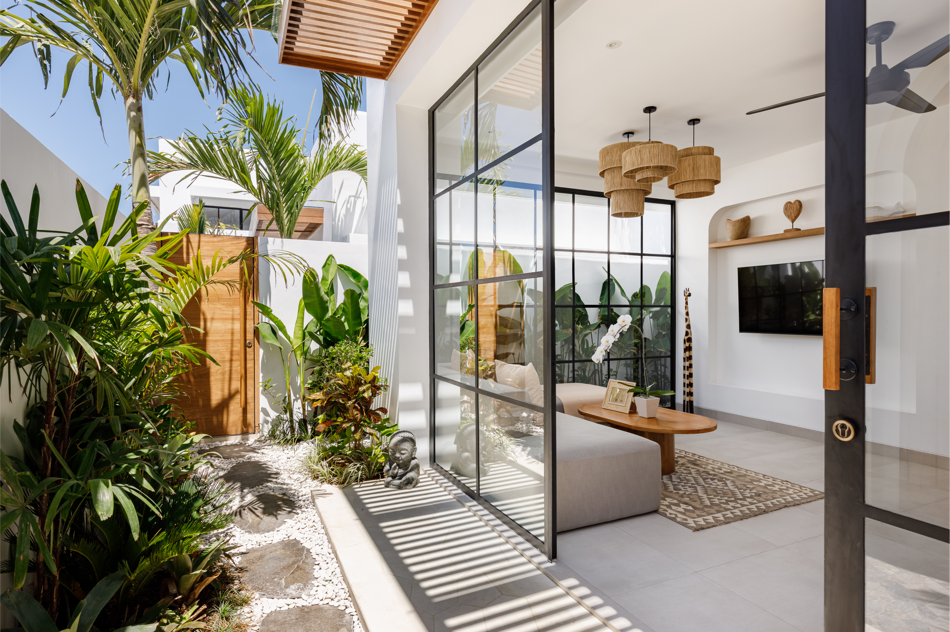 Open glass doors to a bright modern patio with tropical plants and a wooden bench