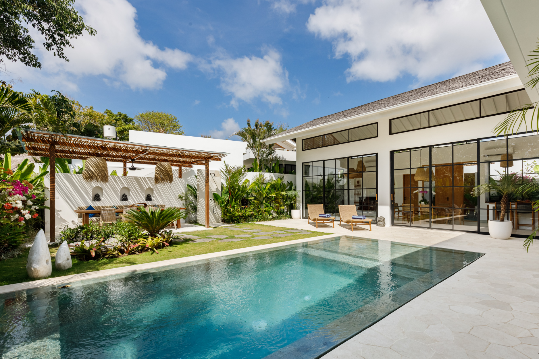 Modern villa patio with turquoise pool, white lounge chairs, pergola, and glass doors