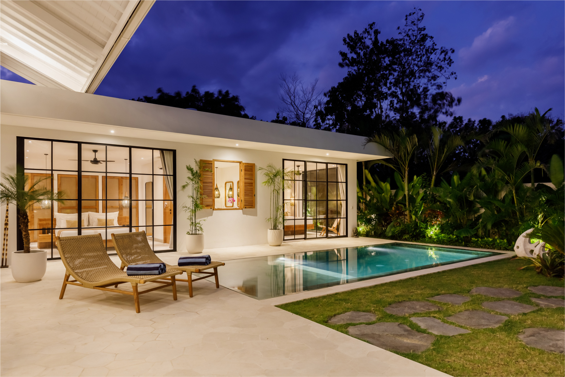 Modern patio with pool, lounge chairs, and warm-lit glass doors at dusk