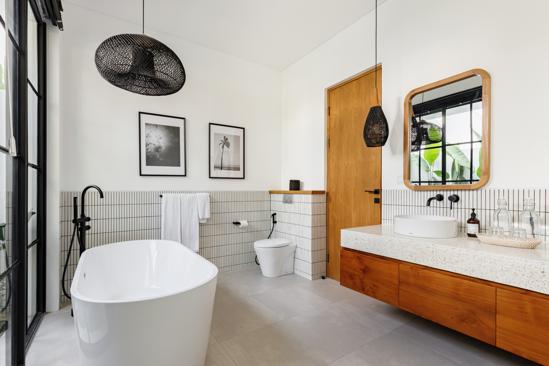 Modern bathroom with freestanding tub, wood vanity, toilet, and white tile walls