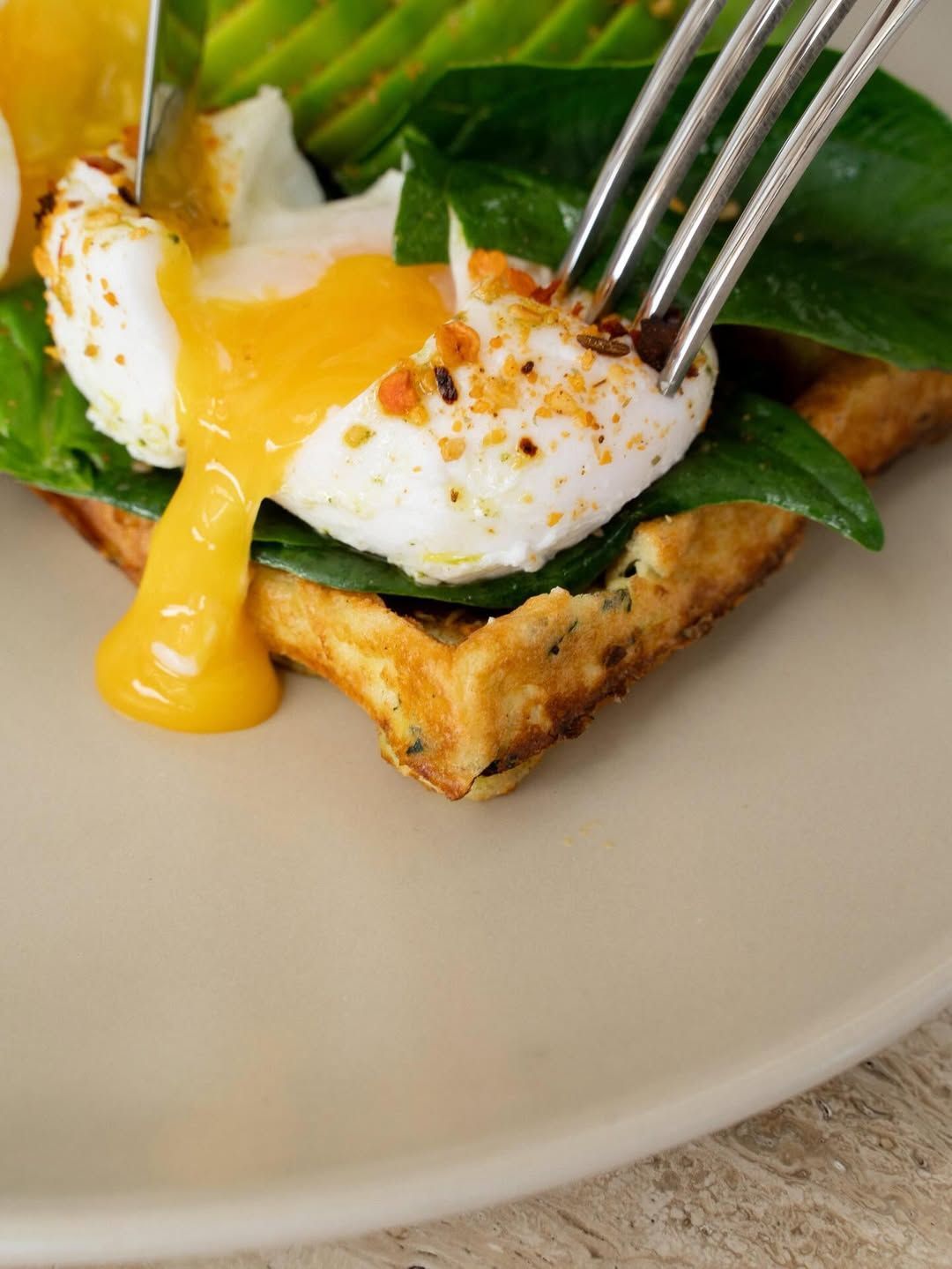 Poached egg on toast with greens and melted yolk, pierced by a fork