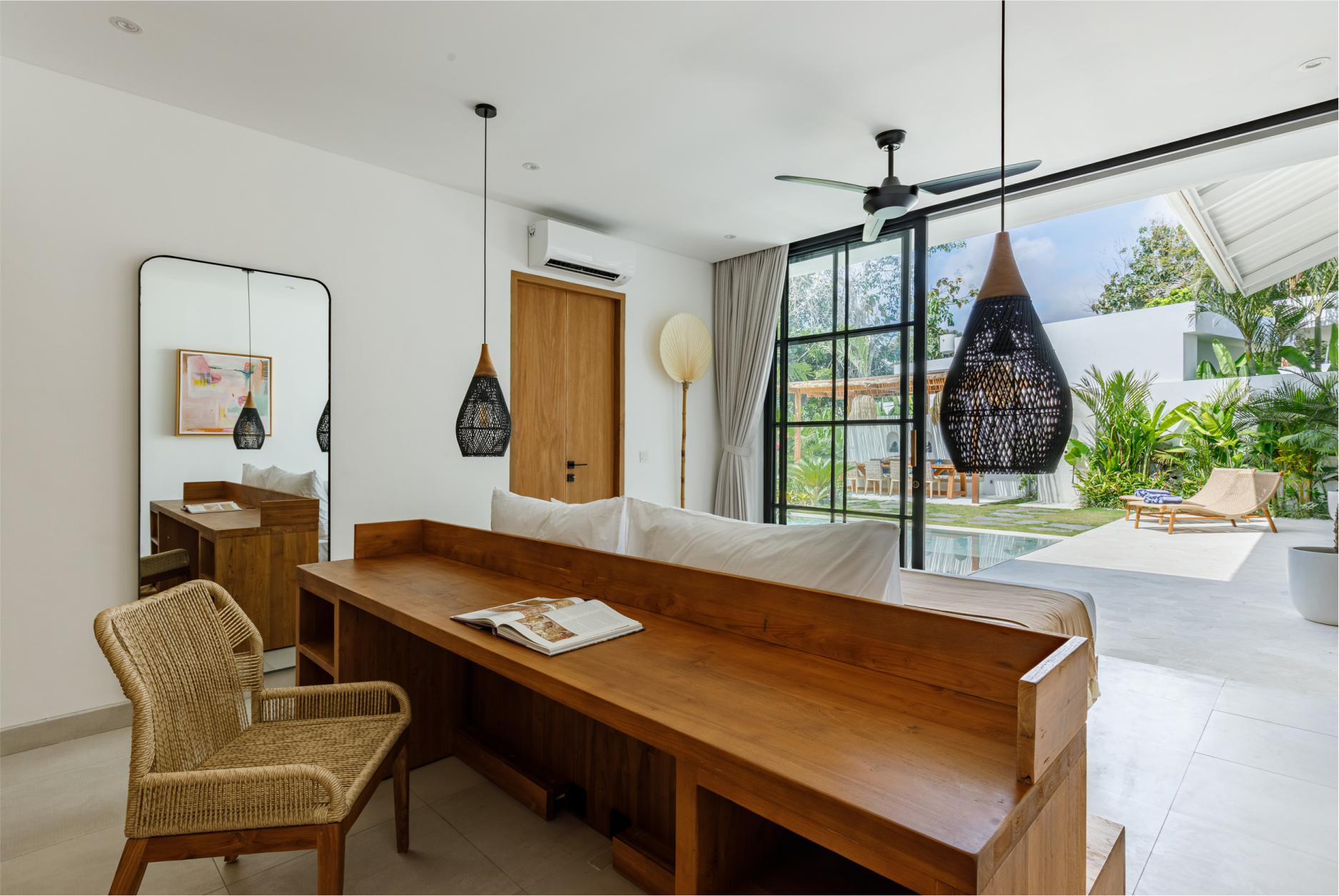 Bright open dining and living room with wooden table, woven chair, and large glass doors to a patio garden