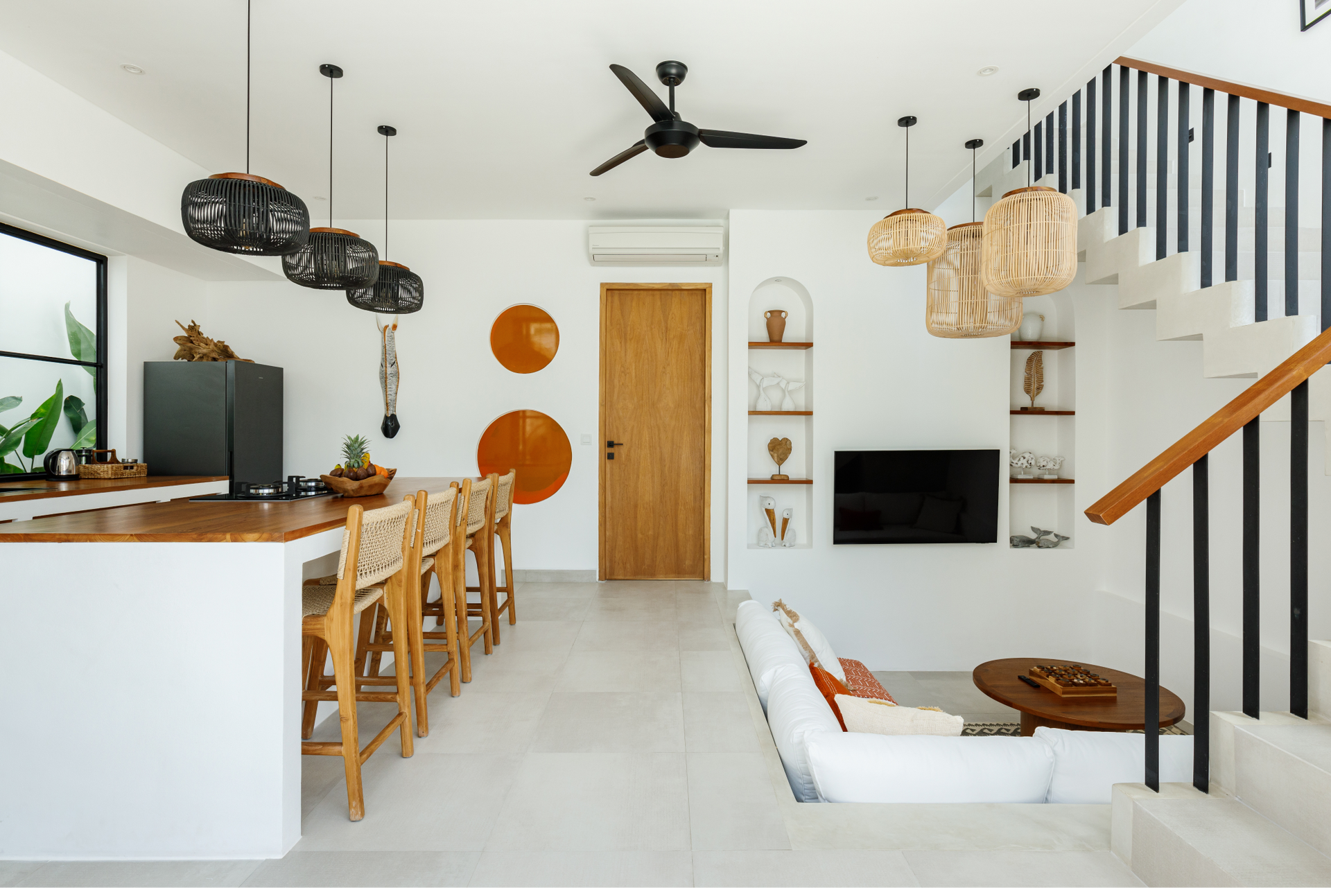Bright modern kitchen and living room with bar stools, staircase, pendant lights, and a wooden door