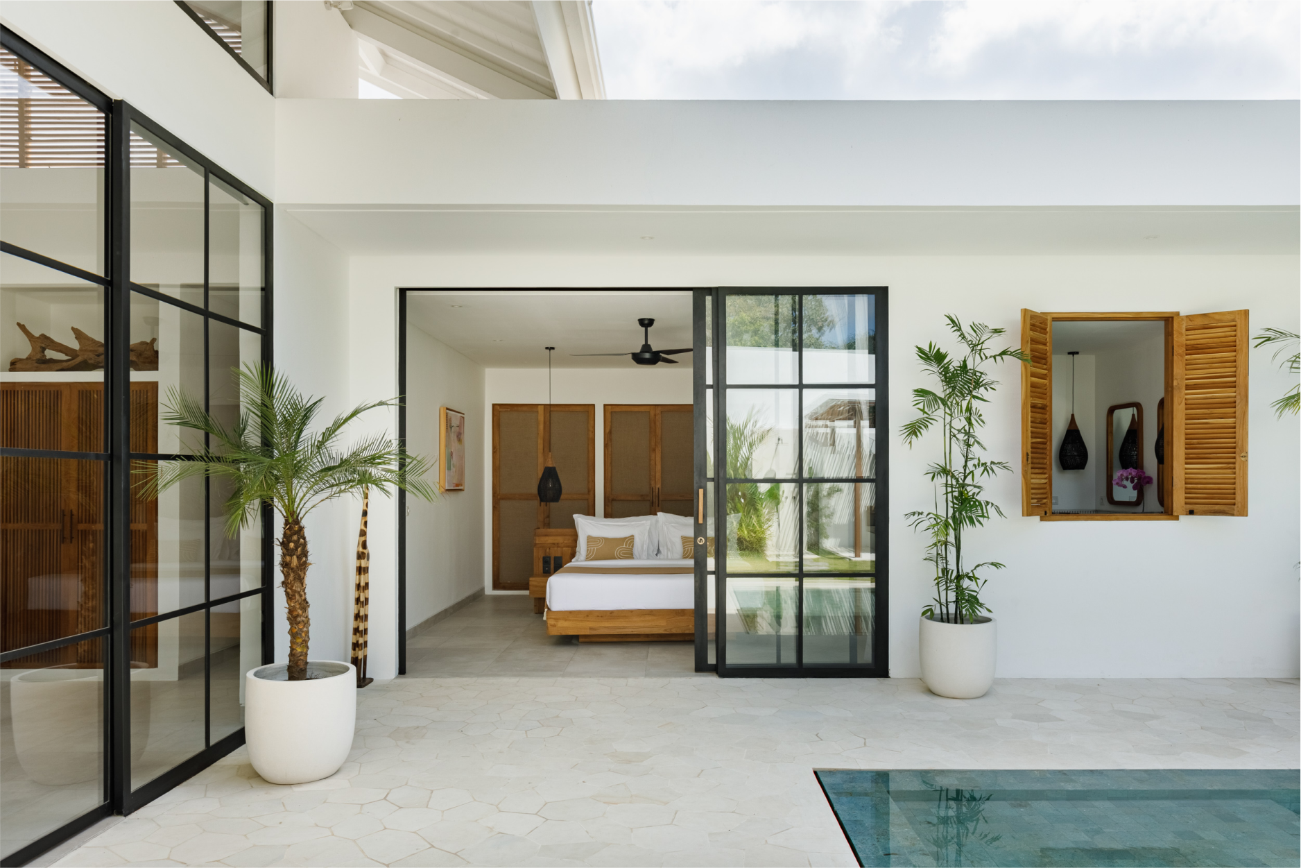 Modern white villa patio with sliding glass doors, bedroom view, potted plants, and pool edge