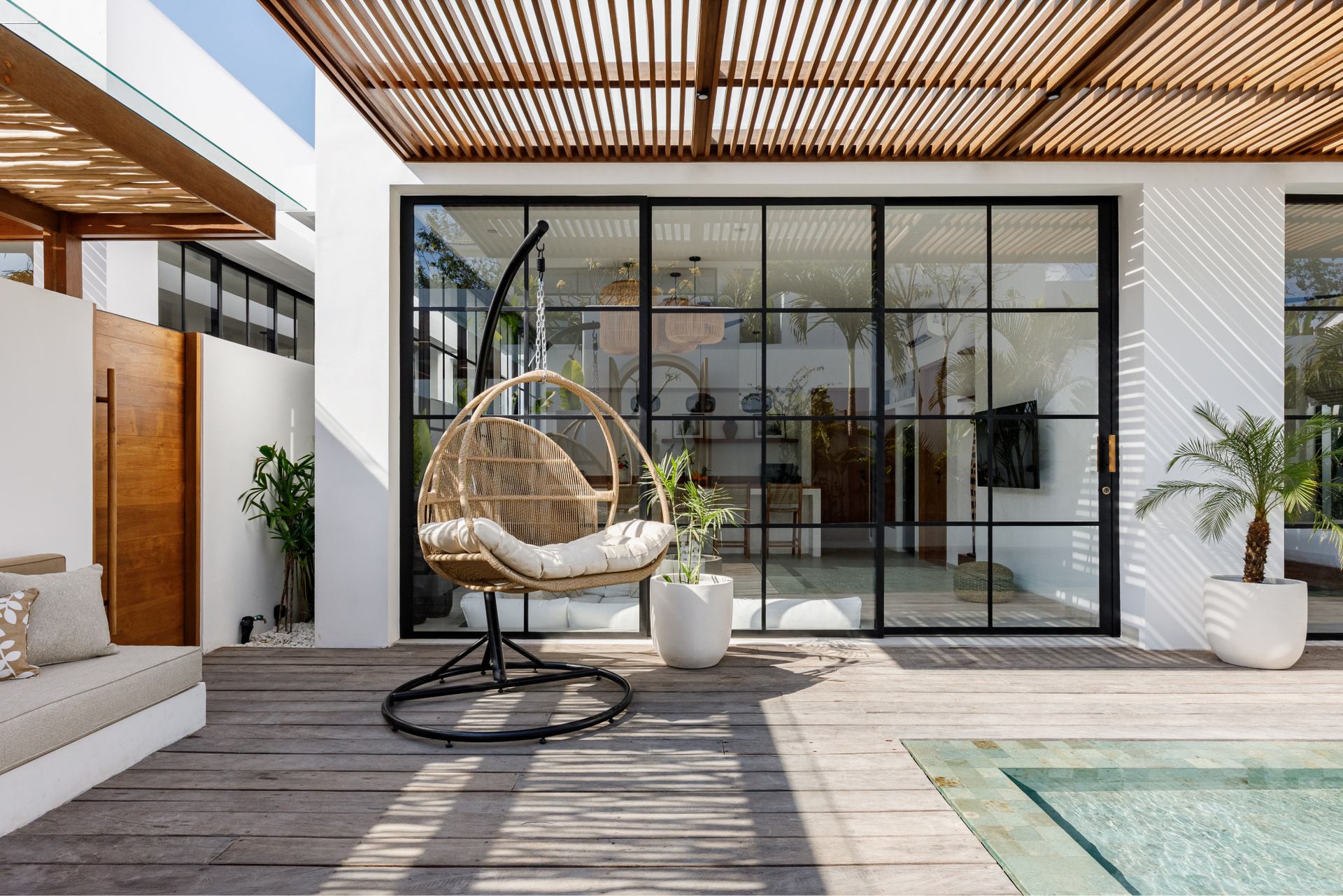 Modern patio with hanging chair, glass doors, wooden pergola, and poolside lounge area
