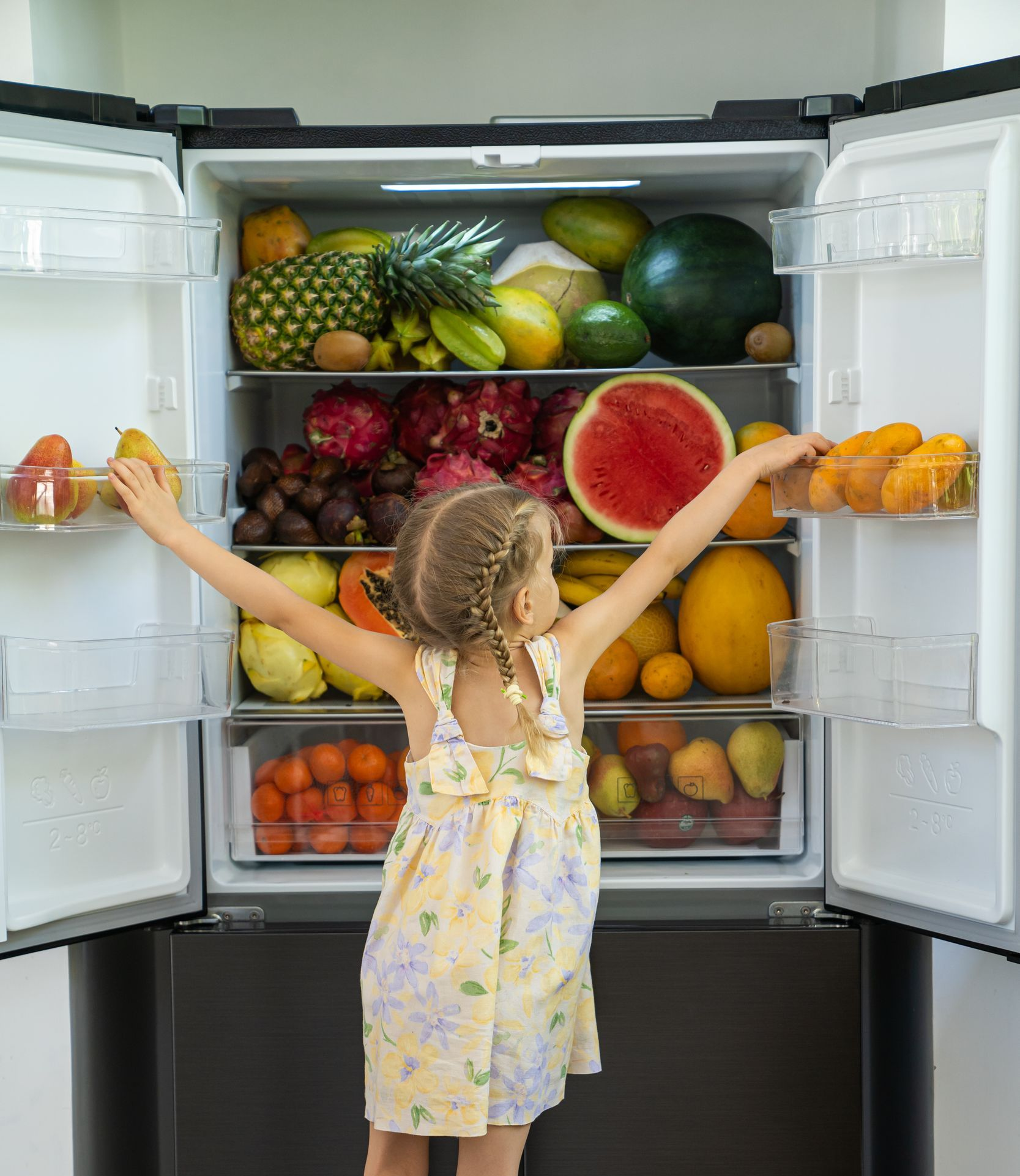Child reaching into an open refrigerator filled with colorful fruits and vegetables