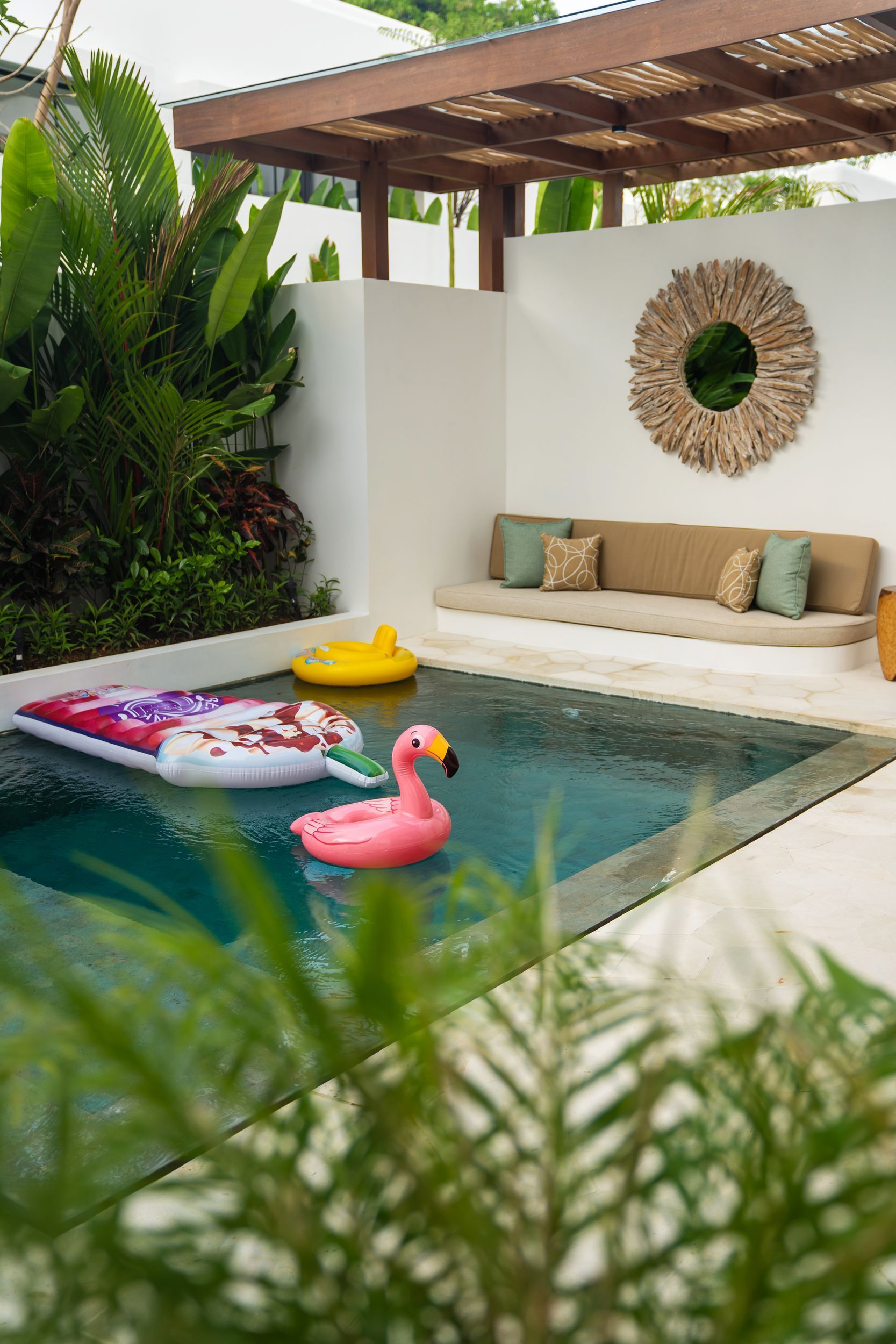 Small patio pool with a tan bench, straw wall mirror, and pink flamingo float under a pergola.
