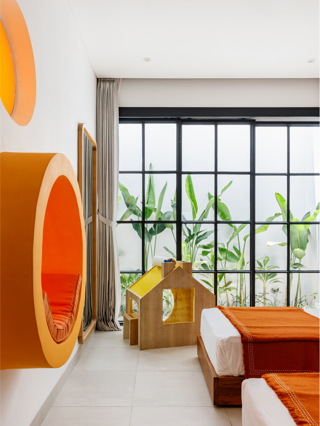 Bright modern room with orange circular wall art, a small wooden playhouse, and a bed by large windows
